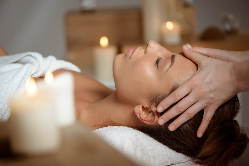 Woman receiving a relaxing head and facial massage in a serene spa setting with candles